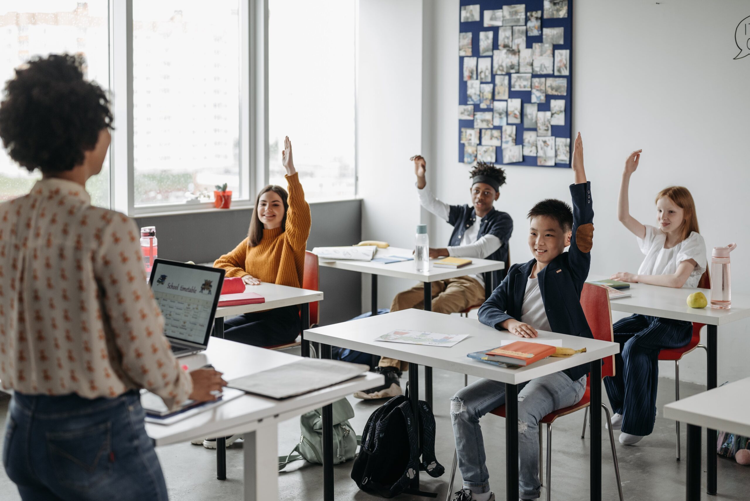 Teacher with students in a classroom raising their hands.